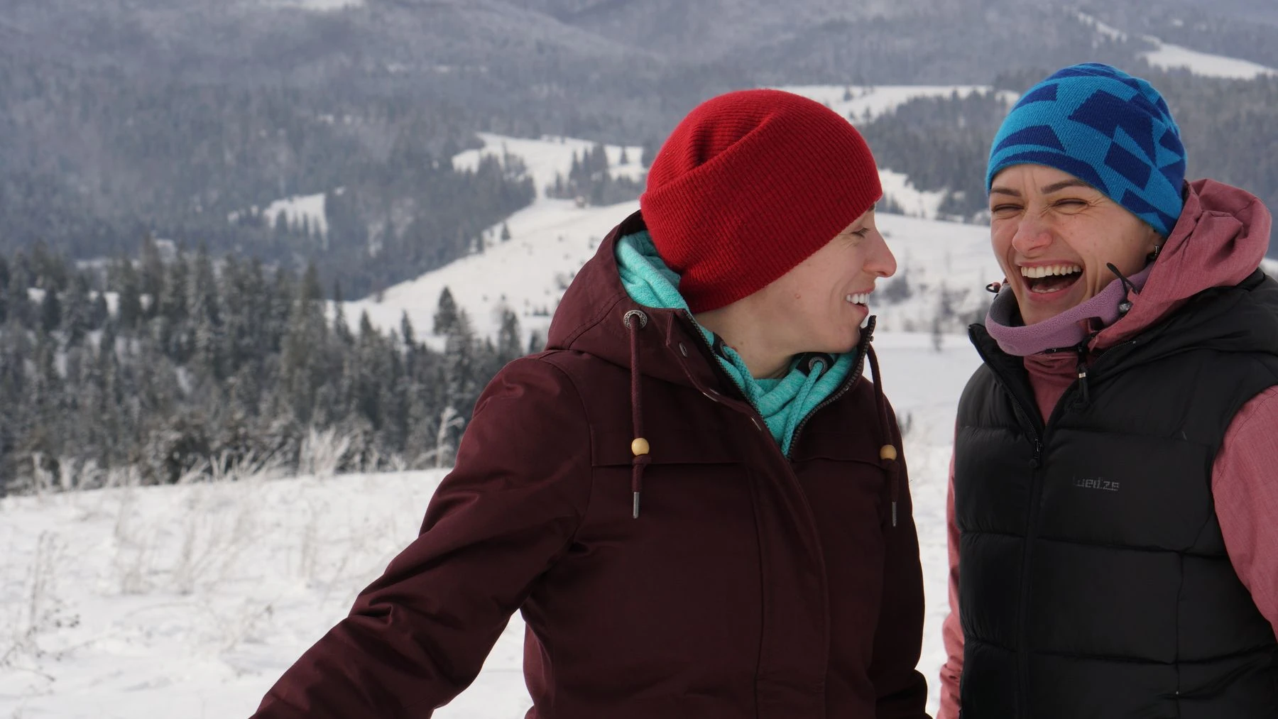 Two friends laughing together outdoors in a snowy mountain landscape