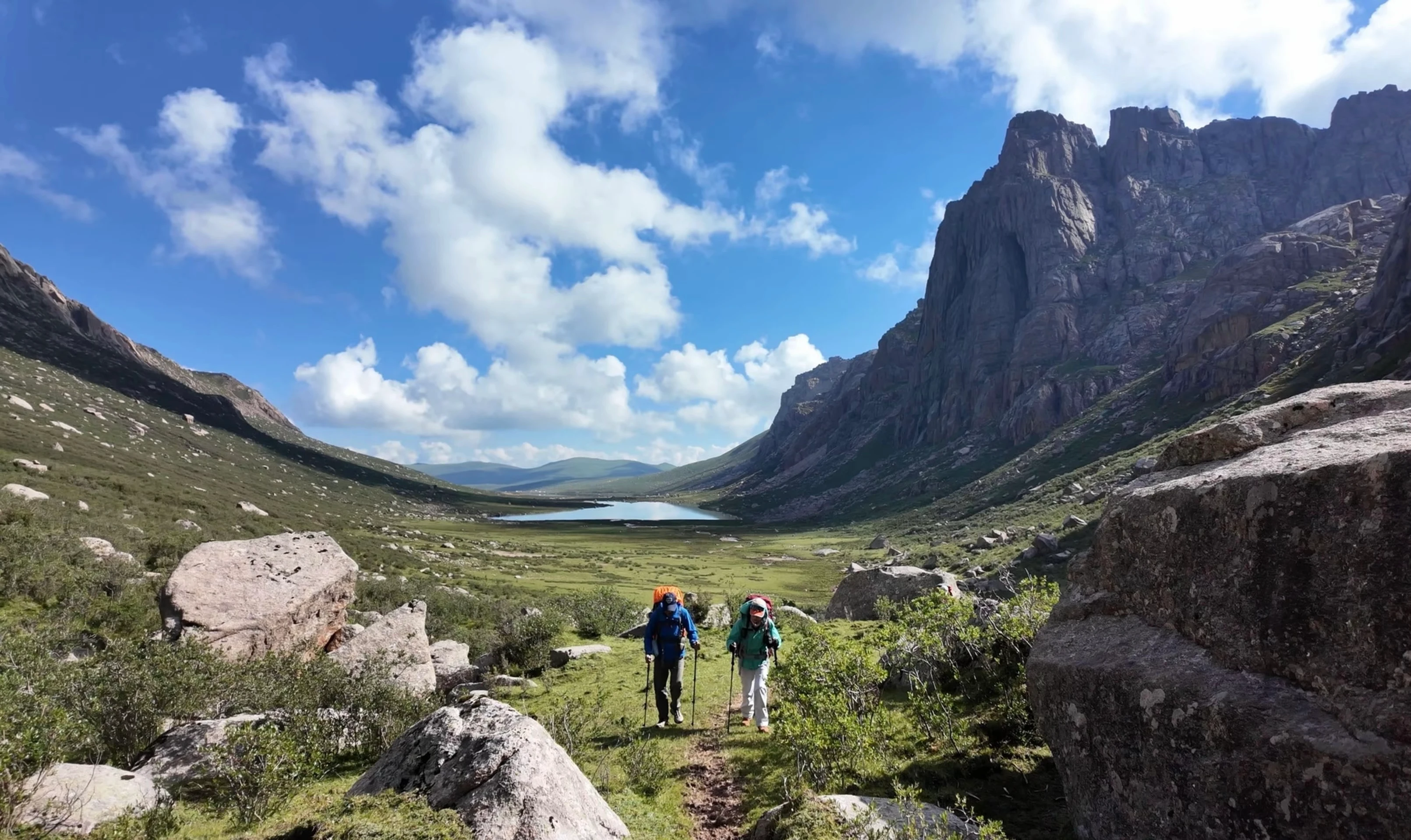 Two hikers with trekking poles on an alpine trail above a mountain valley